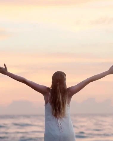 rear view of woman with arms raised at beach during sunset